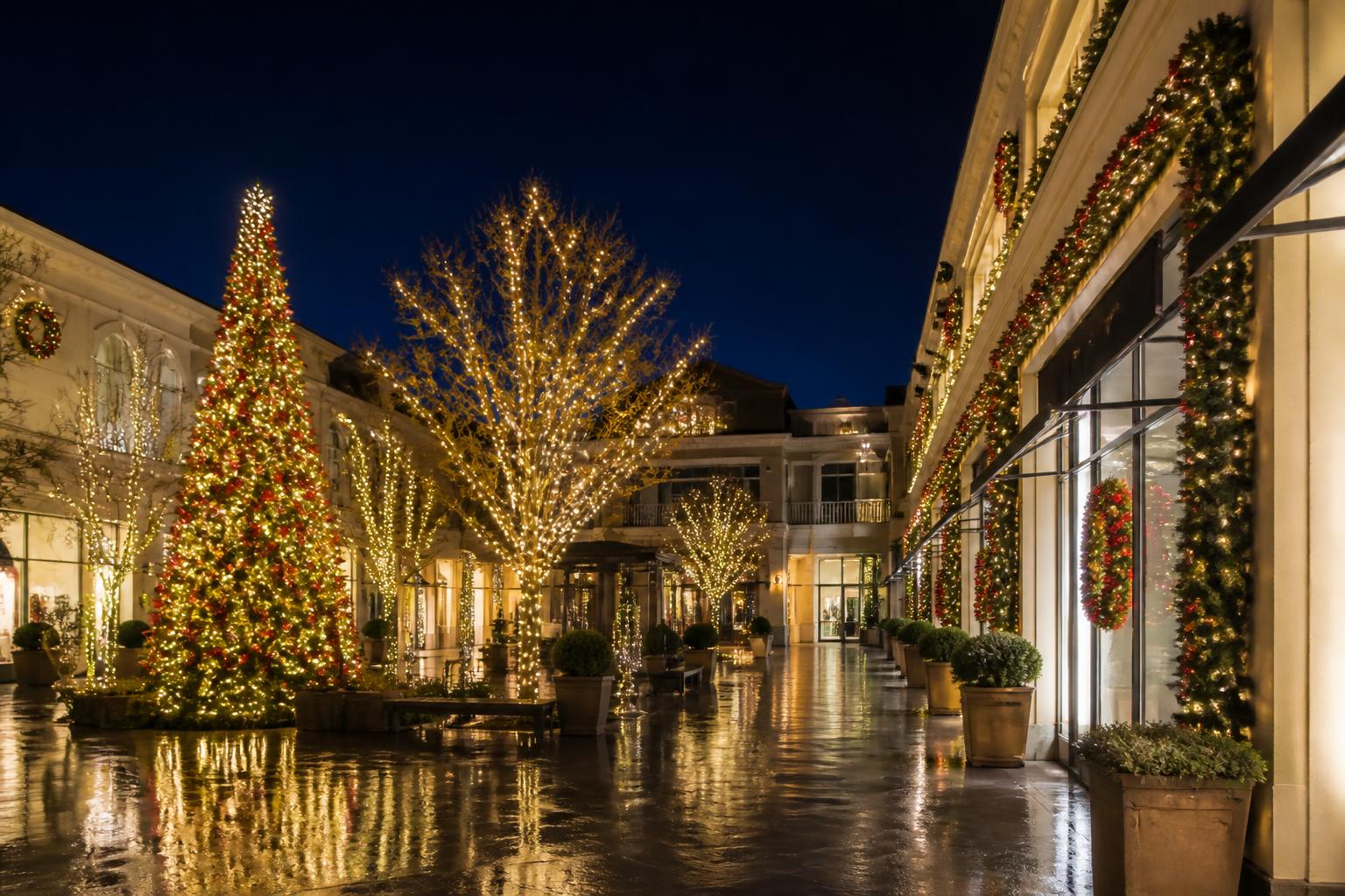 Upscale outdoor shopping center decorated with lit garland, wreaths, wrapped courtyard trees and a large lit Christmas tree